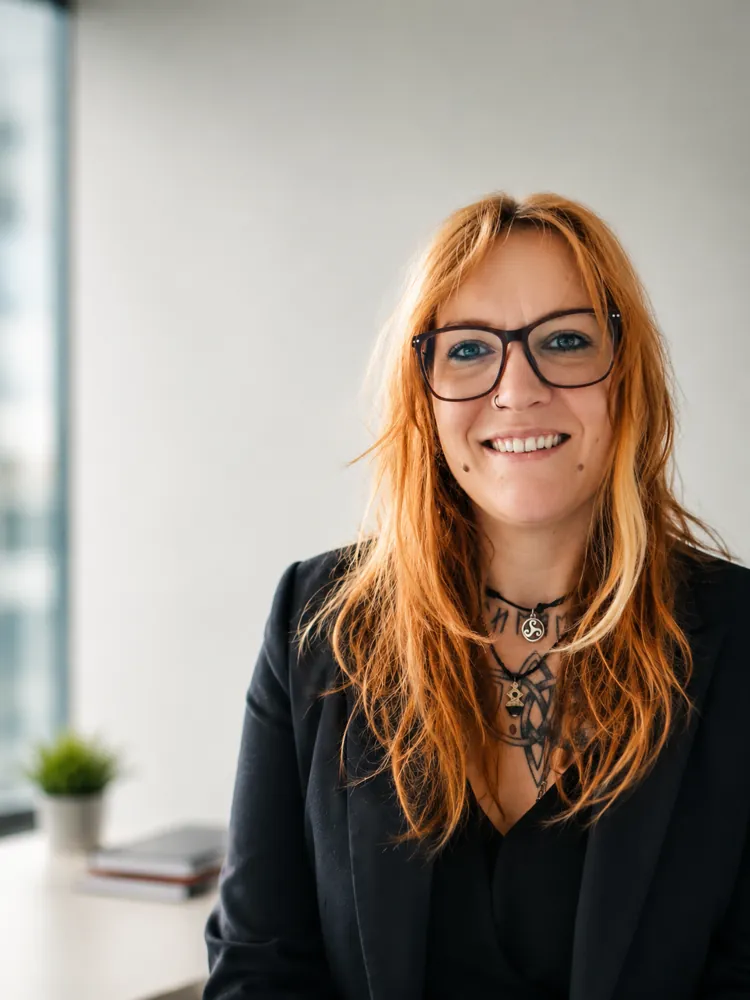 Porträt von Jula Piscart, Gründerin von Mind Unit, lächelnd mit Brille und schwarzem Blazer
